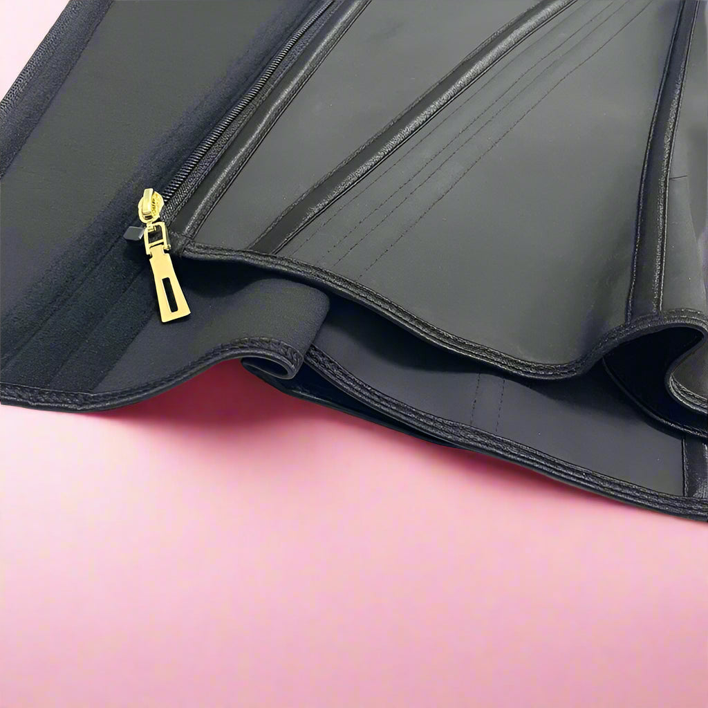 Black waist trainer with a gold zipper on a pink background